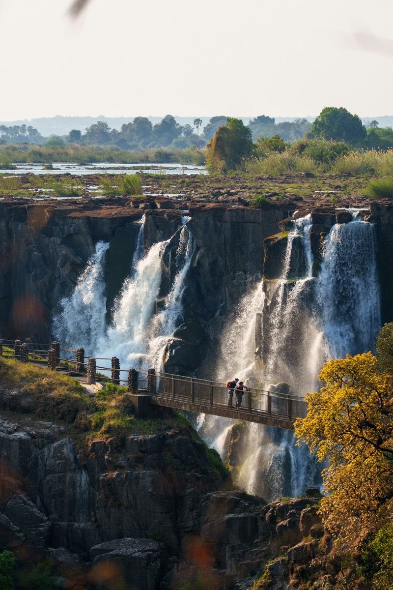 Visitors on the viewing bridge at Victoria Falls overlooking the roaring curtain of waterfalls and misty gorge, Zimbabwe