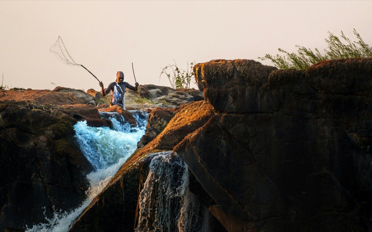 Man fishing with net near waterfall at sunset, Victoria Falls, Zimbabwe