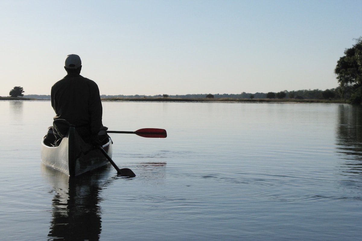 Person paddling a canoe on the calm Zambezi River at dawn in Mana Pools, Zimbabwe