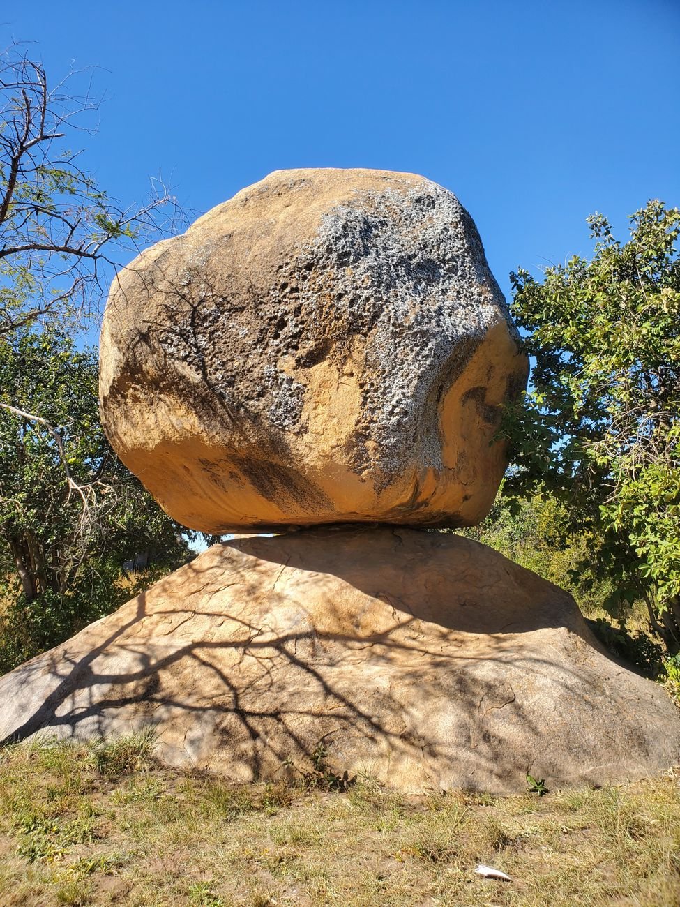 A granite balancing rock on a sandy hillside under a clear blue sky, Epworth, Zimbabwe
