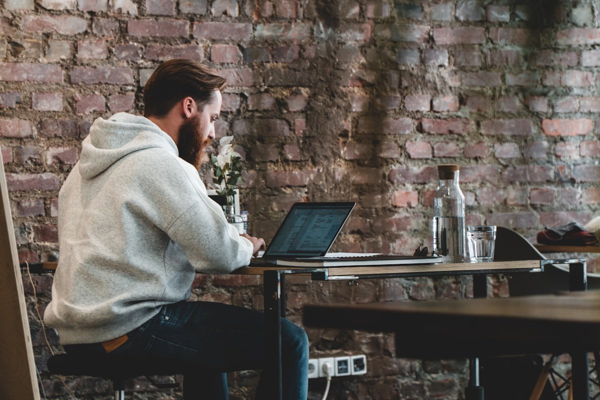 Man working on laptop at a desk in a brick-walled cafe environment