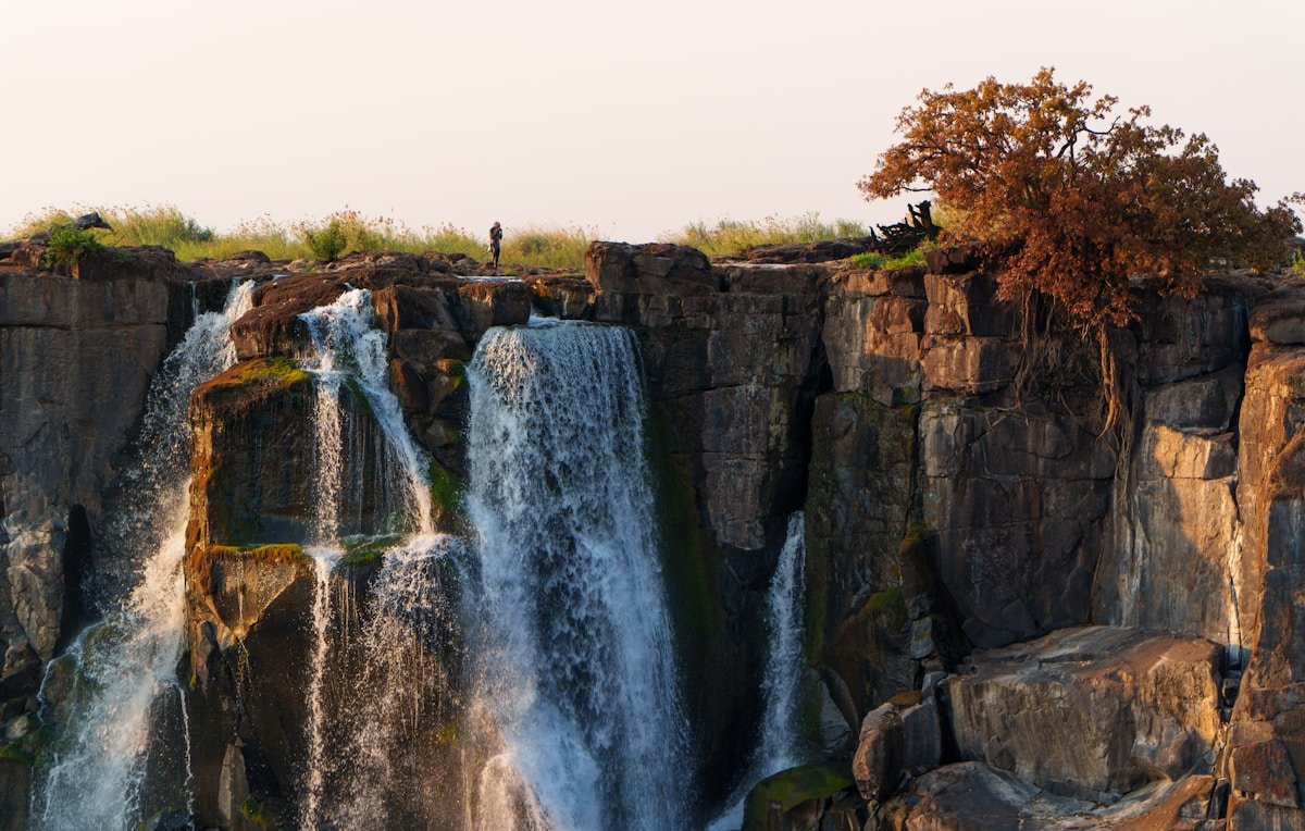 Solo traveller standing on the rocky edge of Victoria Falls gorge with cascading waterfalls, Zimbabwe