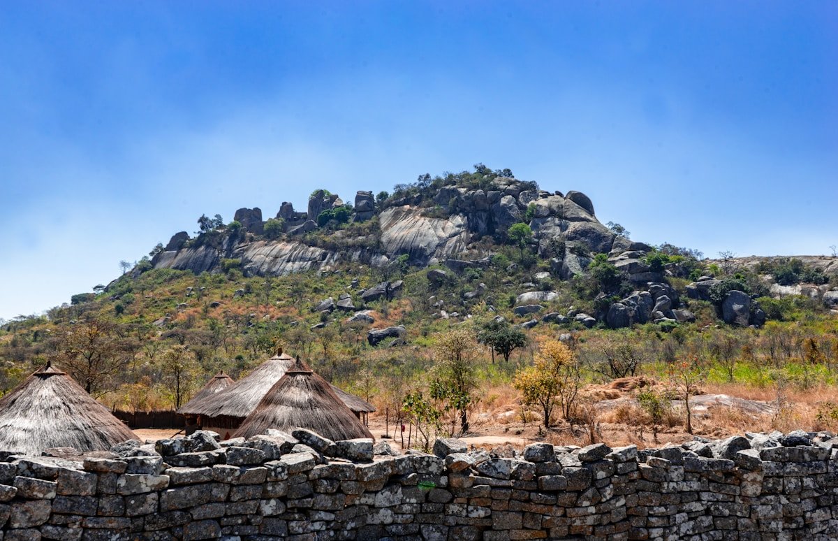 The granite Hill Complex of Great Zimbabwe rising above ancient stone walls and traditional thatched buildings