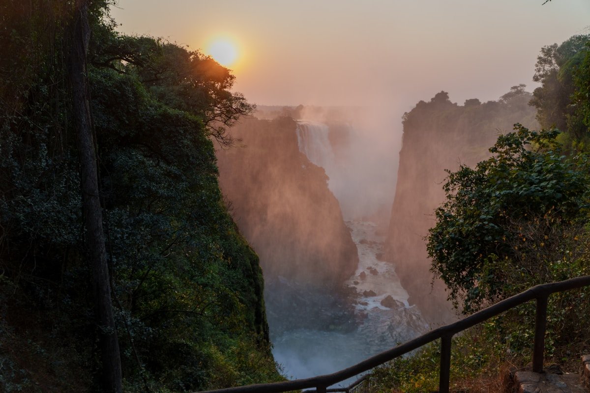 Sunrise through mist over Victoria Falls gorge with lush vegetation and the Zambezi River below