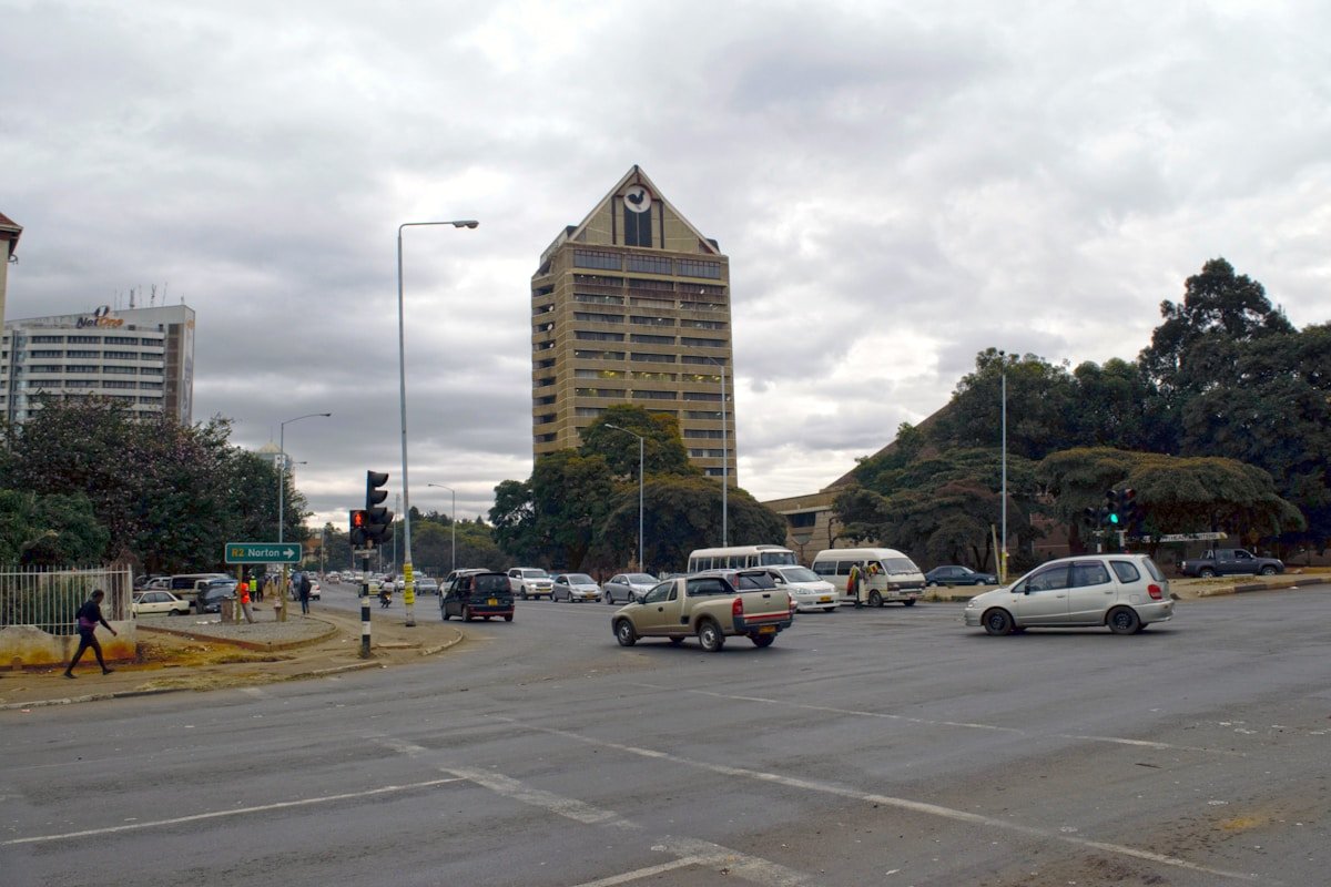 A busy city street intersection in central Harare, Zimbabwe, with traffic and tall buildings