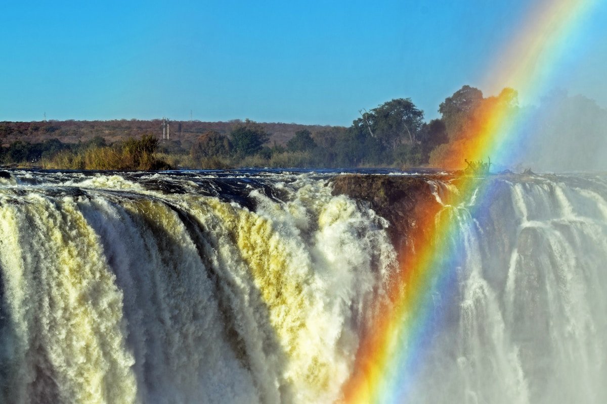 Victoria Falls with a rainbow arching over the rushing water under a clear blue sky