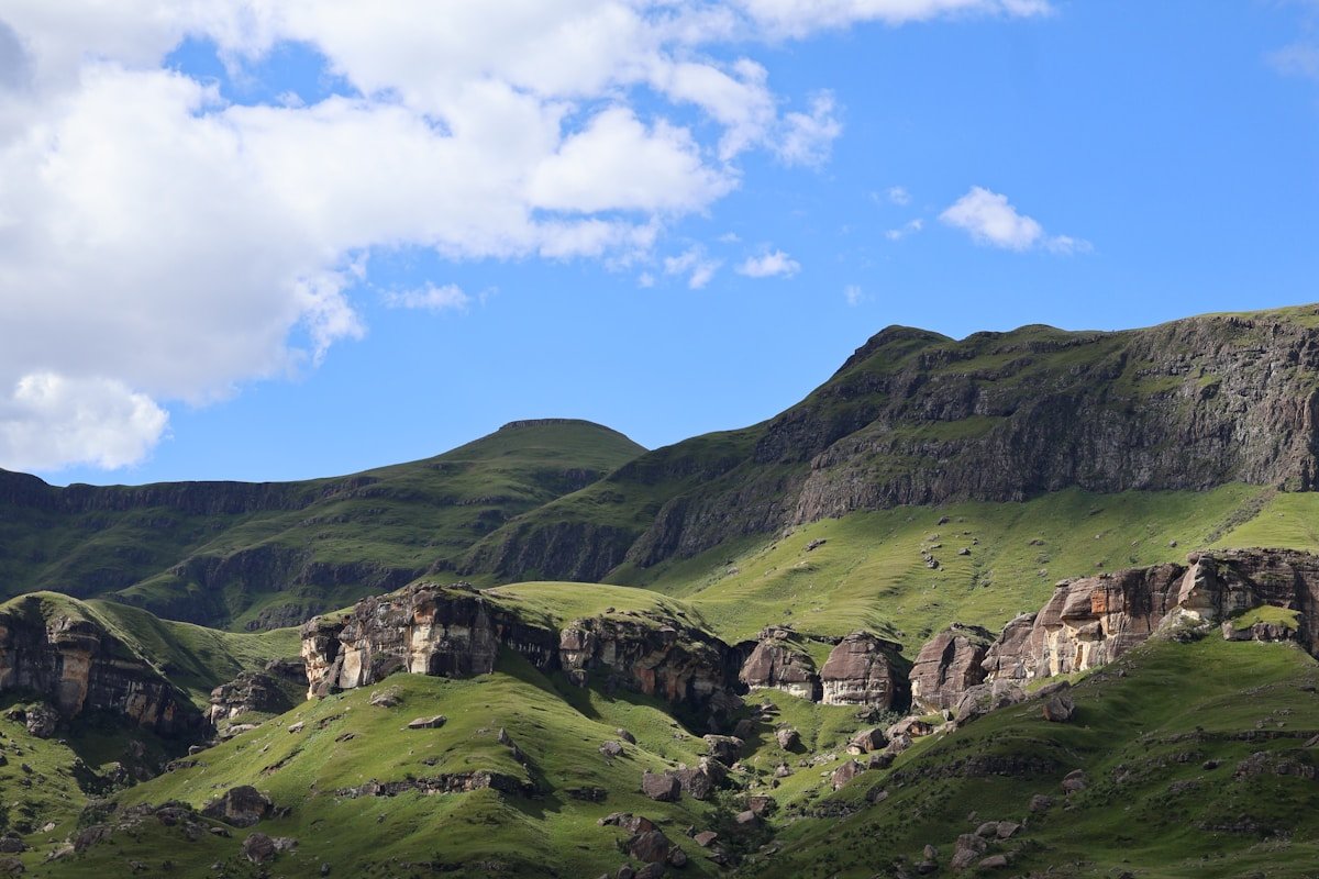 Dramatic green mountain slopes with rocky sandstone cliffs and ridgelines rising under a blue sky in southern Africa