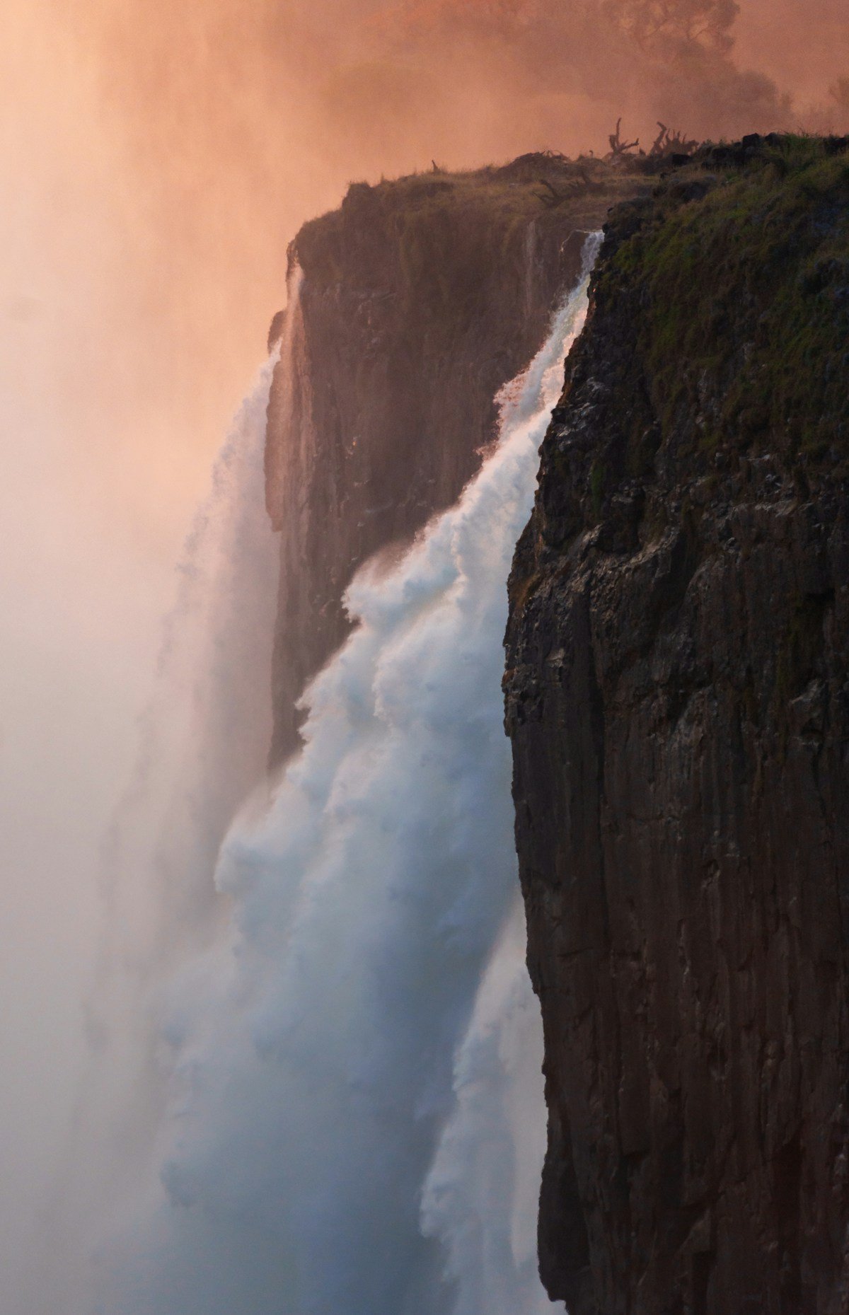 A powerful waterfall cascades down rugged rocky cliffs at sunset in the Eastern Highlands of Zimbabwe