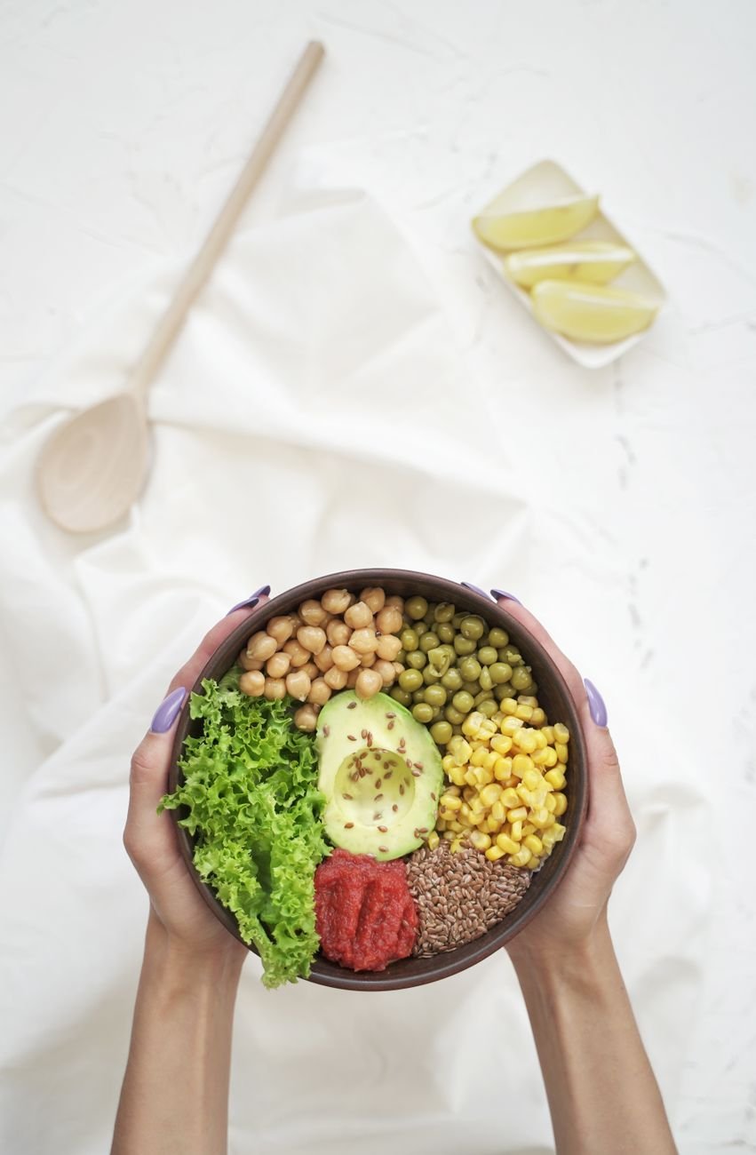 Woman holding a delicious vegan bowl with avocado, chickpeas, corn, and greens